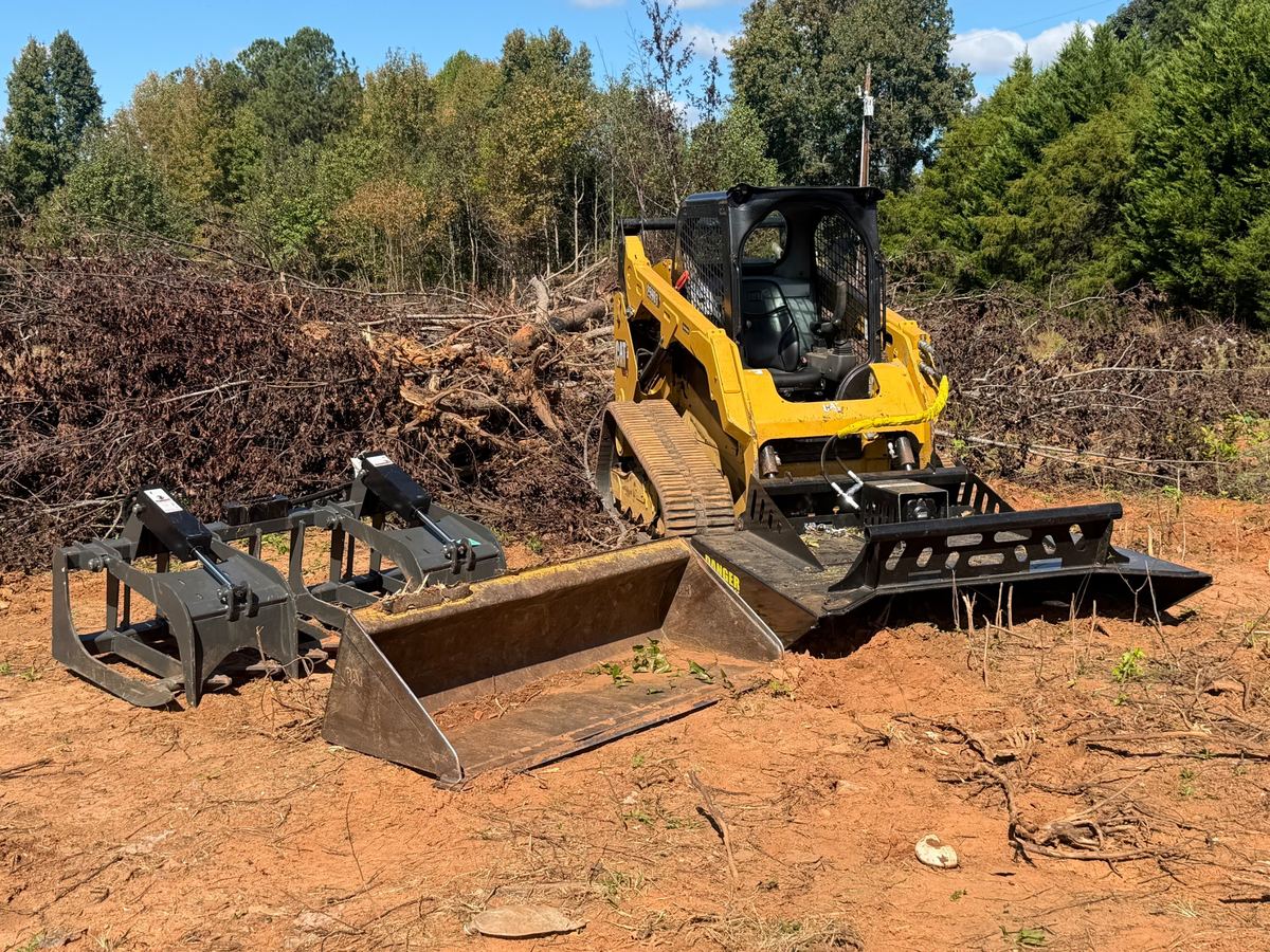 Southern Land Services loader on a freshly cleared lot of red clay, with brush piled behind it.